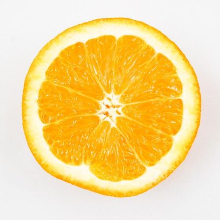 Ein Nahaufnahme einer geschnittenen Orange mit leuchtend gelben Segmenten und weißem Mark auf weißem Hintergrund.