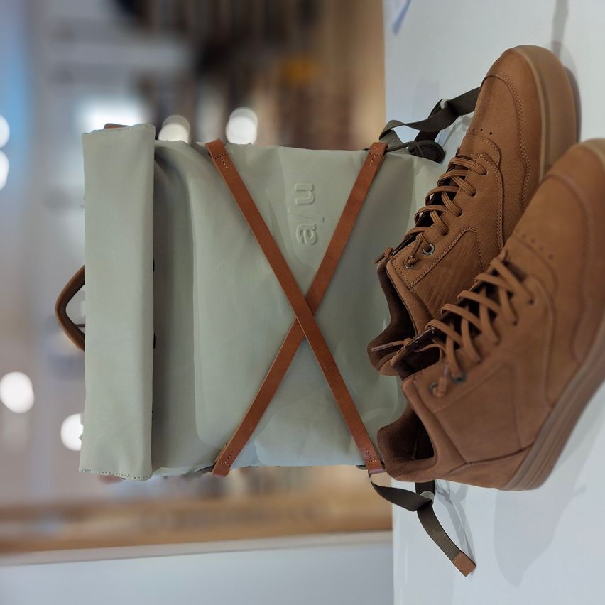 Ein Paar braune Lederstiefel mit Schnürsenkeln ist an einer Wand montiert, neben einer grauen Tasche mit braunen Riemen.