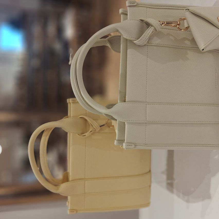 Two beige leather handbags are displayed on a white background. One has a smaller, slightly darker beige bag attached to it.