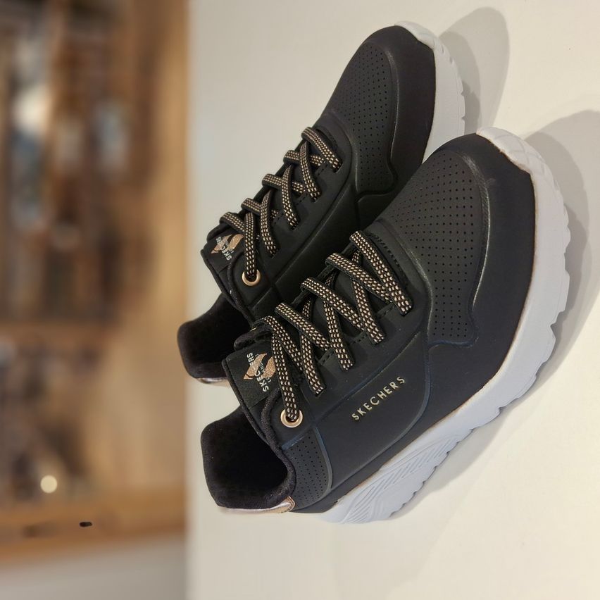 Ein Paar schwarze und weiße Skechers-Sneaker mit goldenen Schnürsenkeln werden auf einem weißen Hintergrund präsentiert.