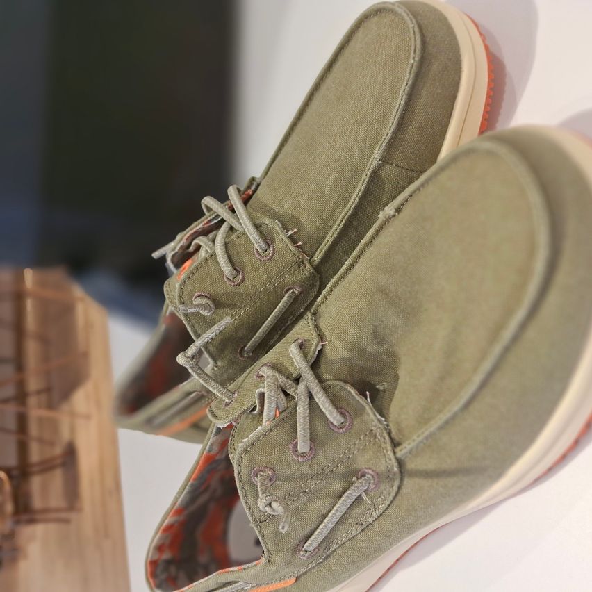 Ein Paar olivgrüne Schuhe mit orangefarbenen Sohlen, vor weißem Hintergrund präsentiert, verfügt über ein  Canvas-Obermaterial und Schnürsenkel.