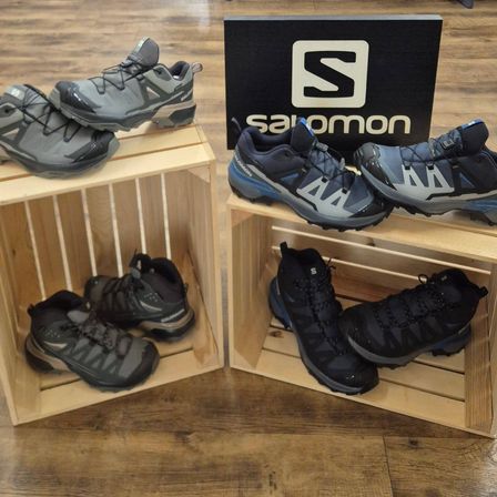 Zwei Holzkisten halten mehrere Paare Salomon-Wanderschuhe, mit einem schwarzen Schild im Hintergrund.