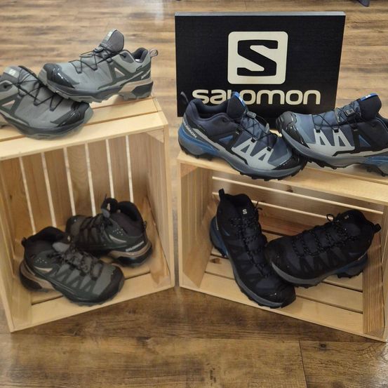 Zwei Holzkisten halten mehrere Paare Salomon-Wanderschuhe, mit einem schwarzen Schild im Hintergrund.