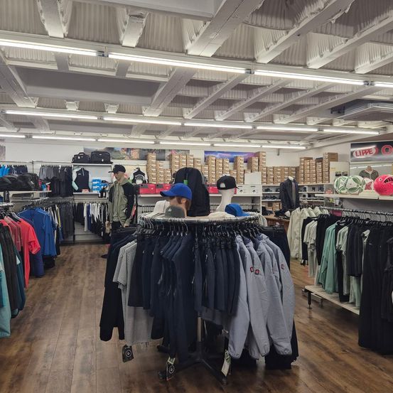 Ein Bekleidungsgeschäft mit einer Vielzahl von Kleidungsstücken an Kleiderbügeln und Regalen. Auch Mannequins und Taschen sind ausgestellt. Die Decke hat mehrere Lichter.