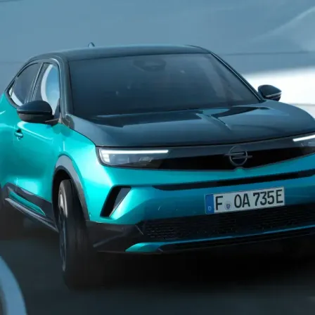 Ein blauer Opel-Wagen mit dem Kennzeichen FO 0A 735E fährt auf einer Straße. Das Auto hat ein schlankes Design mit schwarzem Frontstoßfänger und blauem Körper.