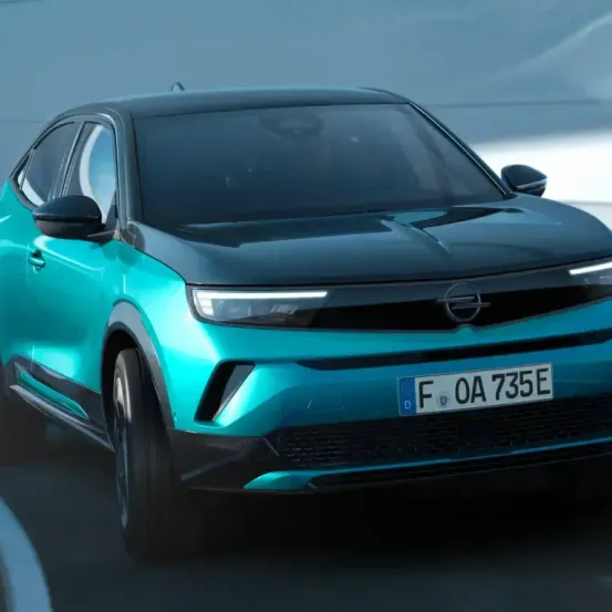 Ein blauer Opel-Wagen mit dem Kennzeichen FO 0A 735E fährt auf einer Straße. Das Auto hat ein schlankes Design mit schwarzem Frontstoßfänger und blauem Körper.
