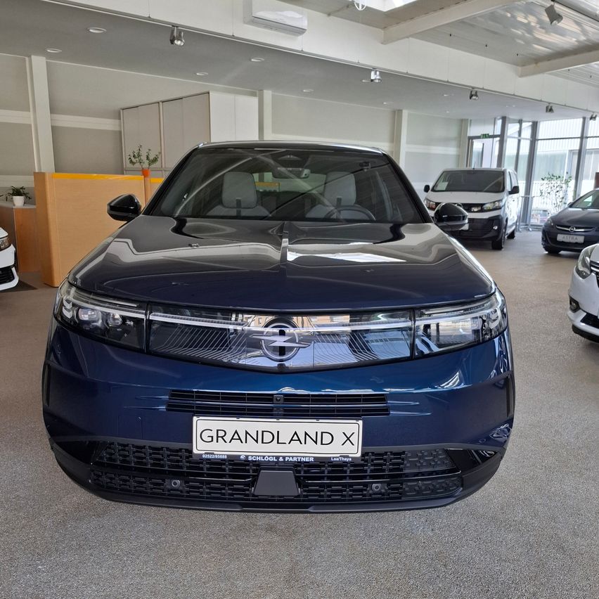 Die Vorderansicht eines blauen Opel Grandland X Elektroautos, das in einem Showroom mit anderen Fahrzeugen geparkt ist.