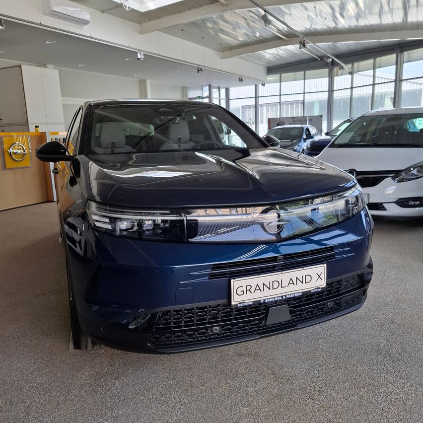 Ein blaues Auto mit dem Kennzeichen GRANDLAND X steht in einem Showroom mit anderen Autos.