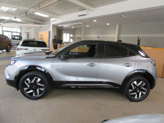 A silver SUV is parked in a showroom with other cars. The car has black tires and silver rims. A man is standing near the car.