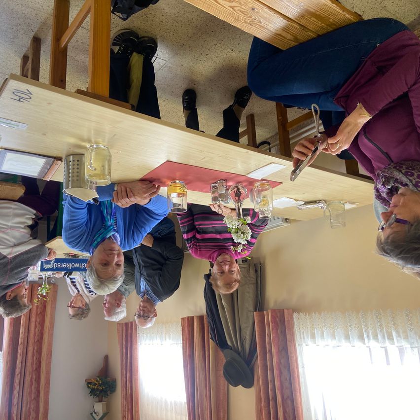 Several people are sitting at a table with glasses, a book, and a flower. They appear to be looking up, perhaps at the camera.