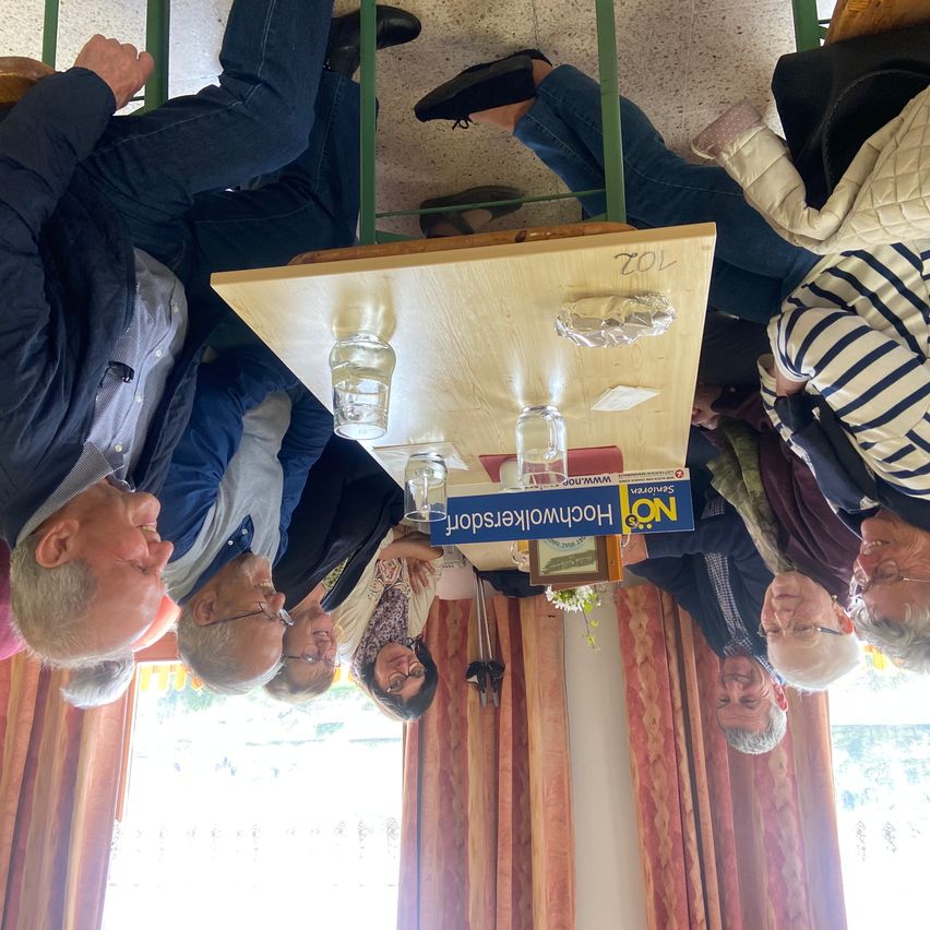 A group of people, upside down, sitting around a table with glasses. A blue sign on the table reads 'Horecamonday'.