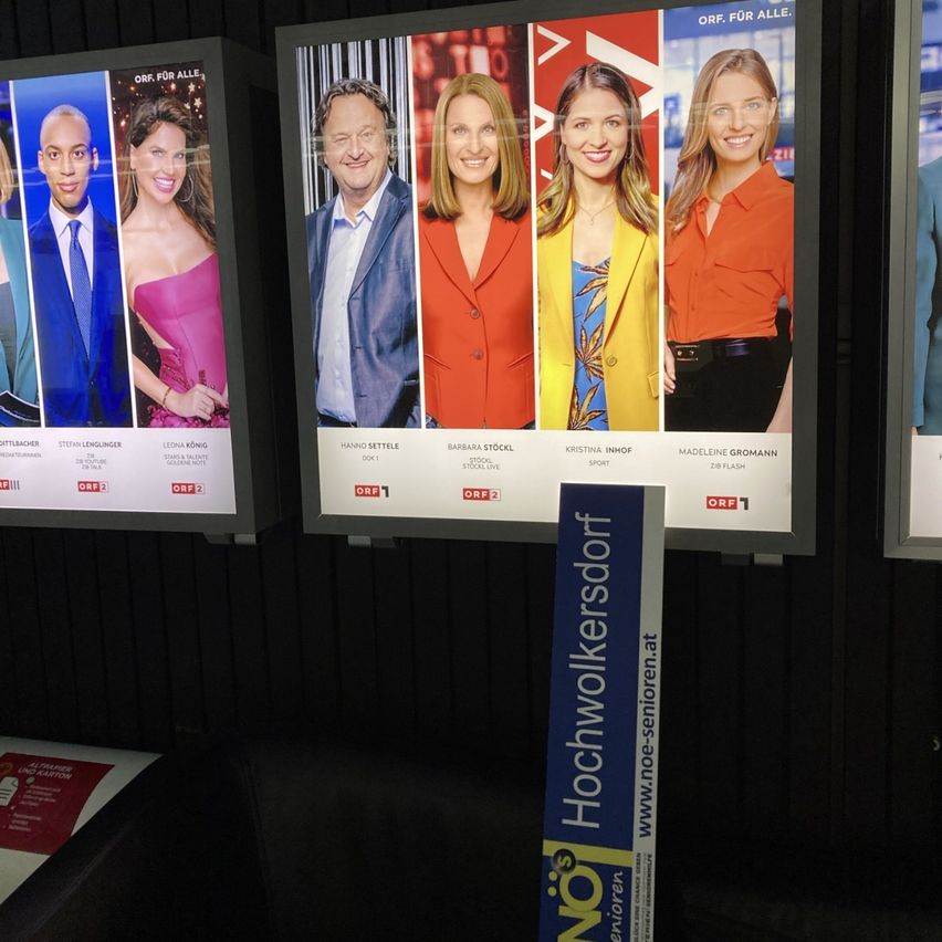 Eine Ausstellung von drei Plakaten mit verschiedenen Menschen in unterschiedlichen Outfits. Das mittlere Plakat hat einen blauen Hintergrund mit weißem Text, der Hochwolkersdof liest.