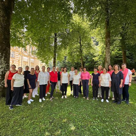 Eine Gruppe von Frauen in verschiedenen Farben posiert für ein Foto in einem Park mit Bäumen und einem Gebäude im Hintergrund.