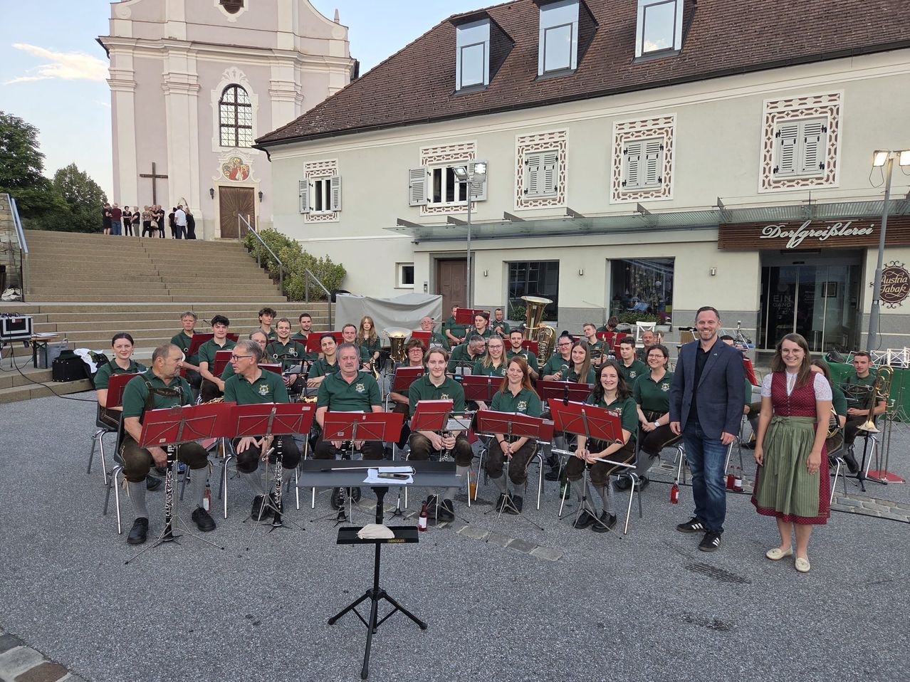 Ein Blasorchester in grünen Uniformen spielt vor einem Gebäude mit einer Kirche im Hintergrund.