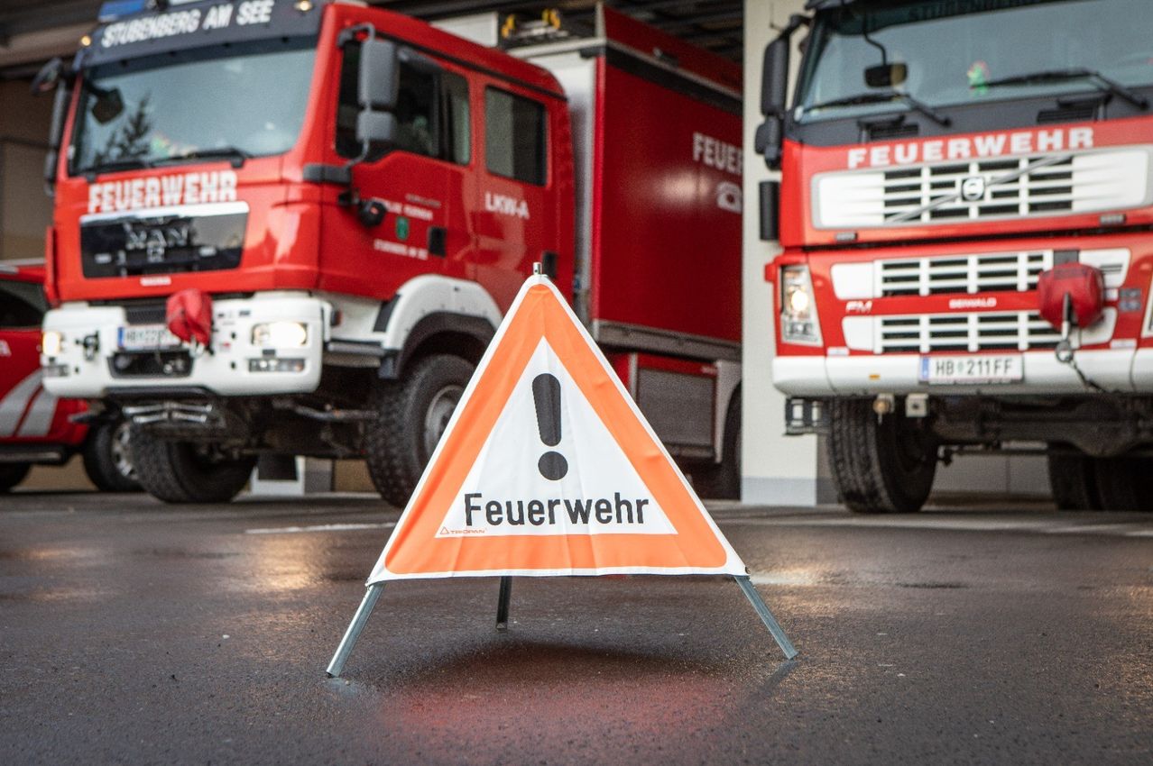 Ein Warnschild der Feuerwehr steht vor geparkten roten Feuerwehrfahrzeugen.