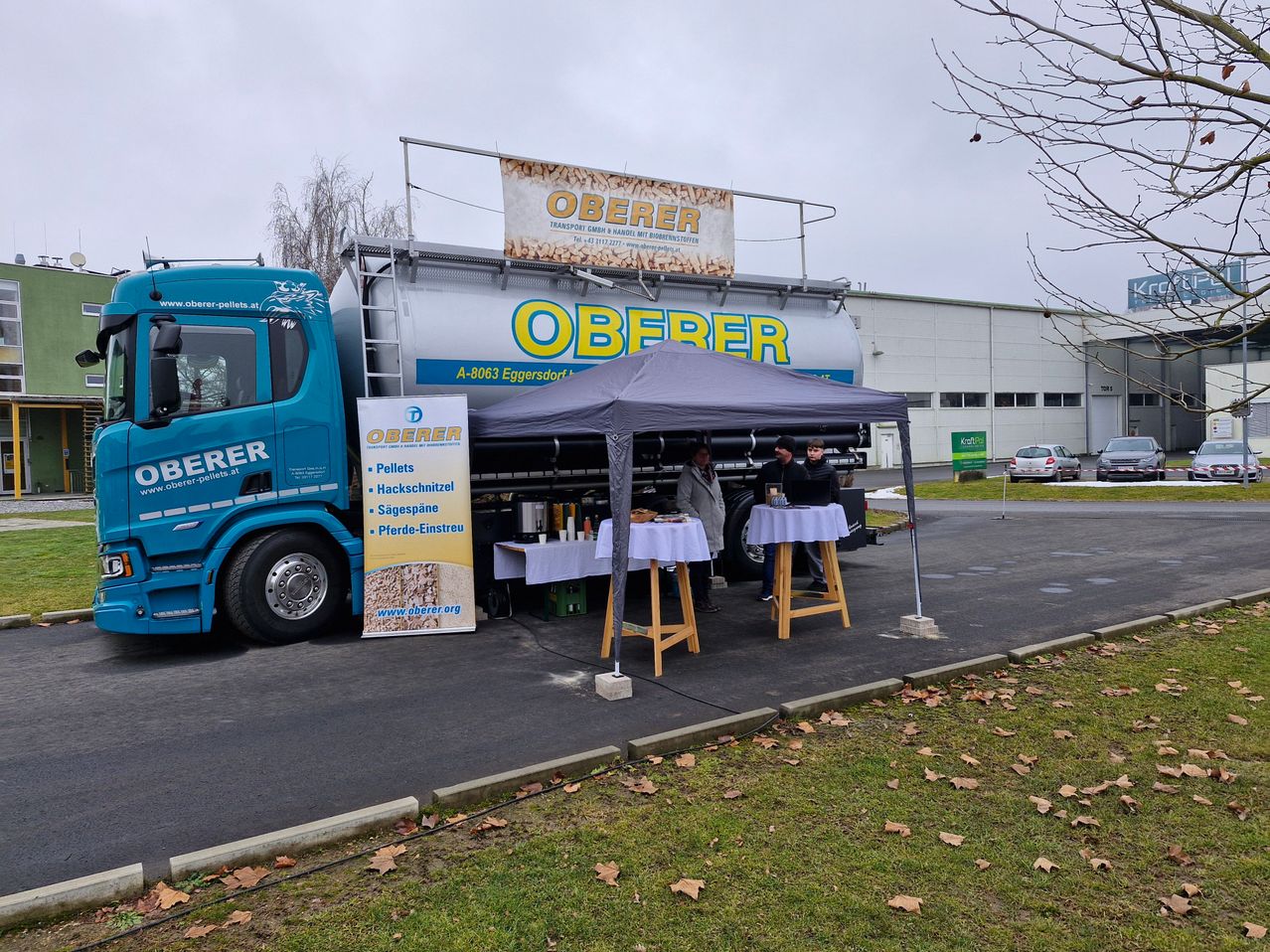 Eine Outdoor-Aufstellung neben einem LKW, möglicherweise für einen Verkauf, mit einem Zelt, Tischen und einem Banner. Ein großer Tankwagen mit dem Wort Oberer ist davor geparkt.