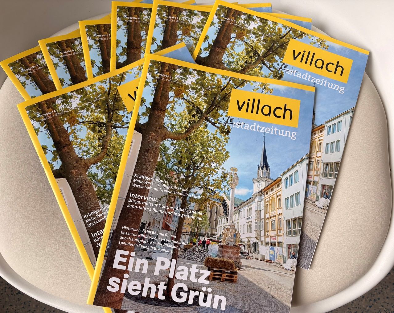 Stapel von vier Zeitschriften mit dem Titel 'Villach Stadtzeitung' mit einem lebhaften Bild eines Baumes und einer Stadtkulisse.