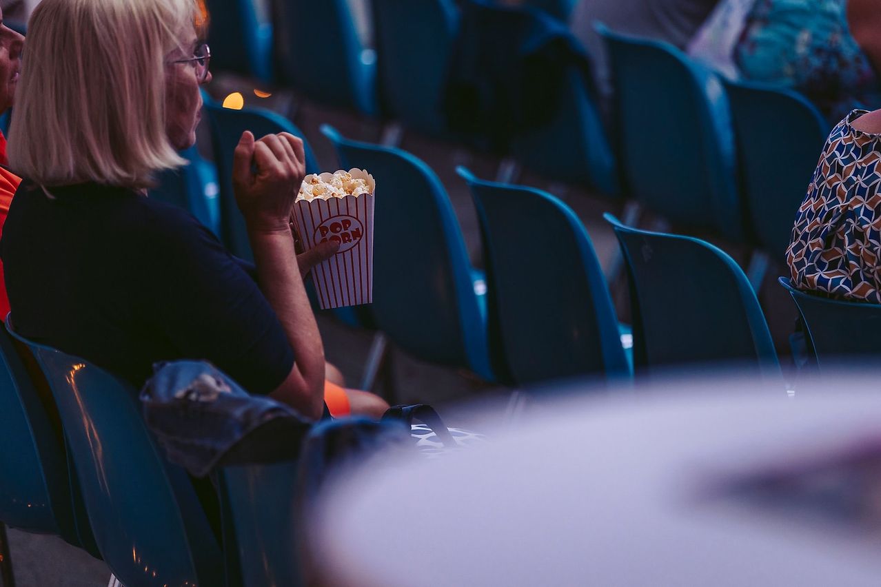 Eine Frau mit Brille sitzt im Kino, hält eine Popcorn-Box und schaut einen Film.