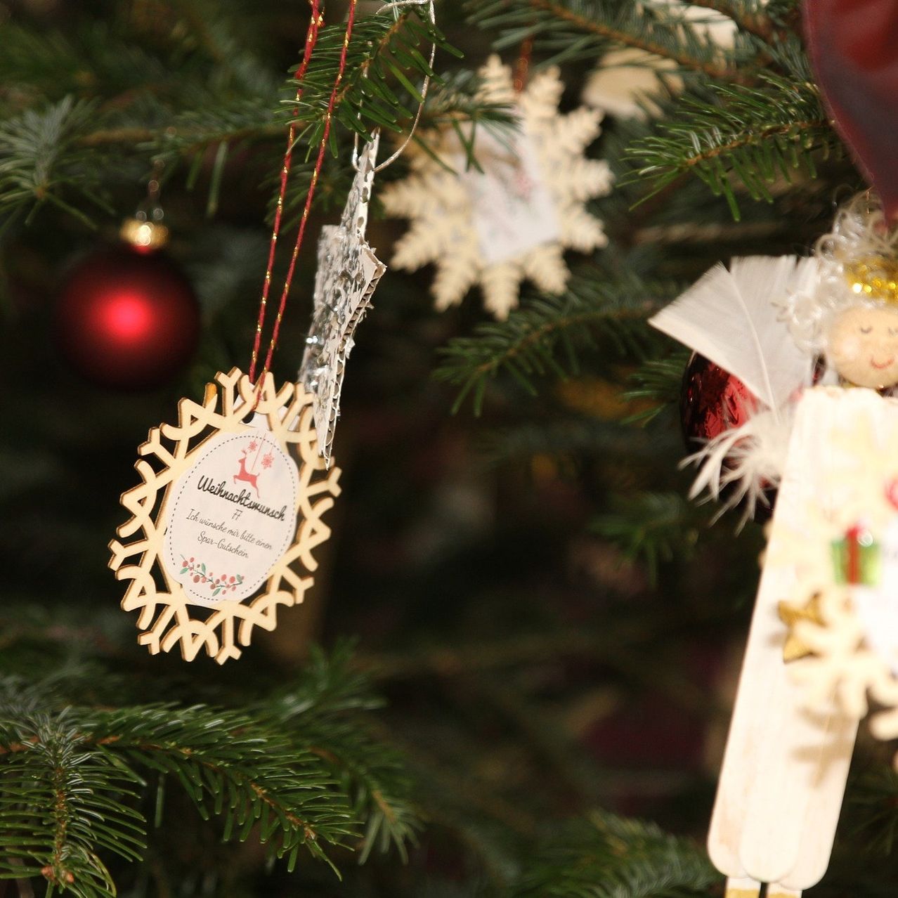 Ein Weihnachtsbaum mit verschiedenen Ornamenten, darunter eine rote Kugel, eine Schneeflocke und eine goldene Schneeflocken-Dekoration mit einer Botschaft sowie einer kleinen Engelsfigur.