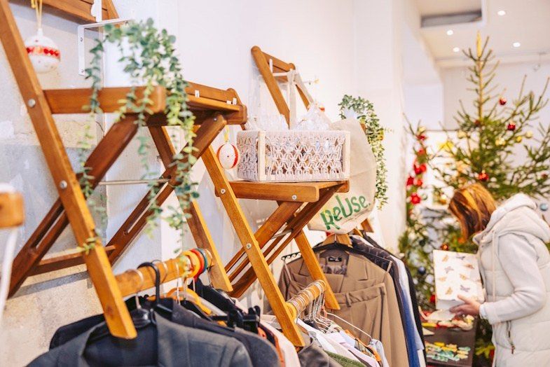 Eine Frau betrachtet eine Geschenkbox vor einem Kleiderständer und einem Weihnachtsbaum.