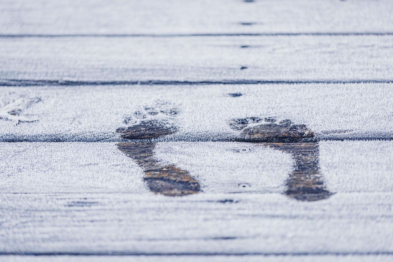 Eine Nahaufnahme einer verschneiten Holzterrasse, die Fußabdrücke und Raureifmuster auf der Oberfläche zeigt.