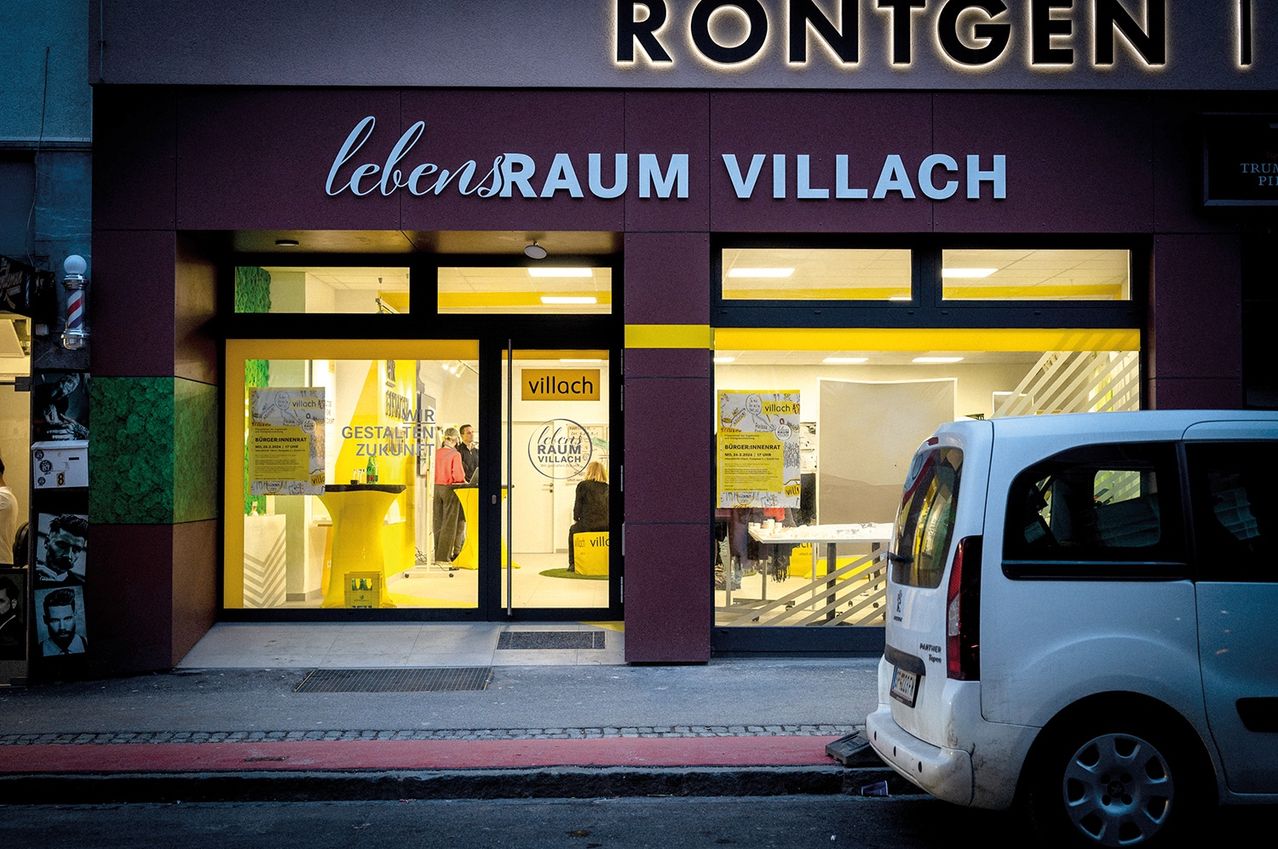 Ein Schaufenster für das Geschäft Rontgen Raum Villach mit Glastüren, Fenstern und einem geparkten weißen Lieferwagen davor.