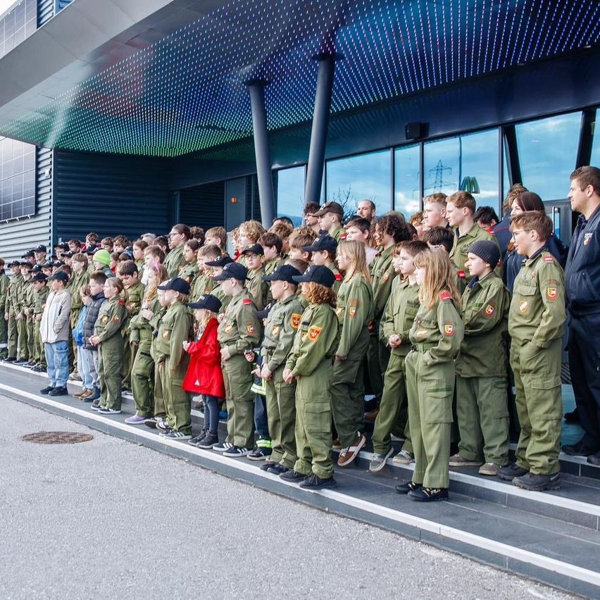 Eine Gruppe von Kindern in Uniformen steht auf Stufen vor einem Gebäude. Ein Erwachsener steht hinter ihnen.