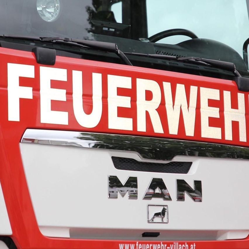 Die rote und weiße Front eines MAN Feuerwehrwagens, mit dem Wort 'FEUERWEHR' in weiß geschrieben. Darunter steht das Wort 'MAN'.
