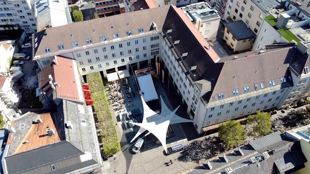 Ein Luftbild einer Stadt mit mehreren Gebäuden, einem großen weißen Baldachin, geparkten Autos und Menschen, die gehen.