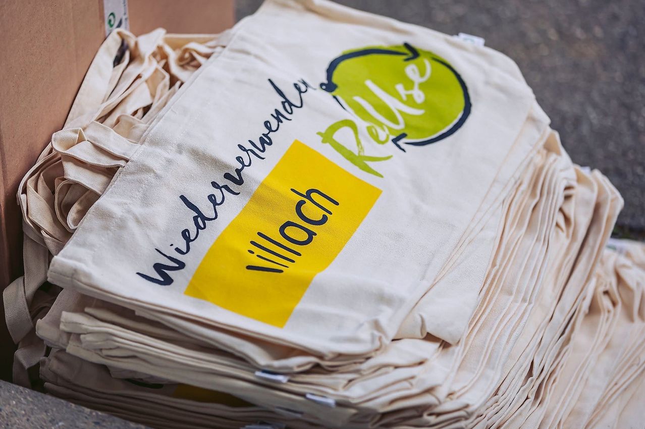 Ein Stapel wiederverwendbarer Taschen mit 'Wiederverwender' und 'Reuse' in Schwarz sowie 'village' in Weiß auf gelbem Hintergrund. Die Taschen sind ordentlich gefaltet.