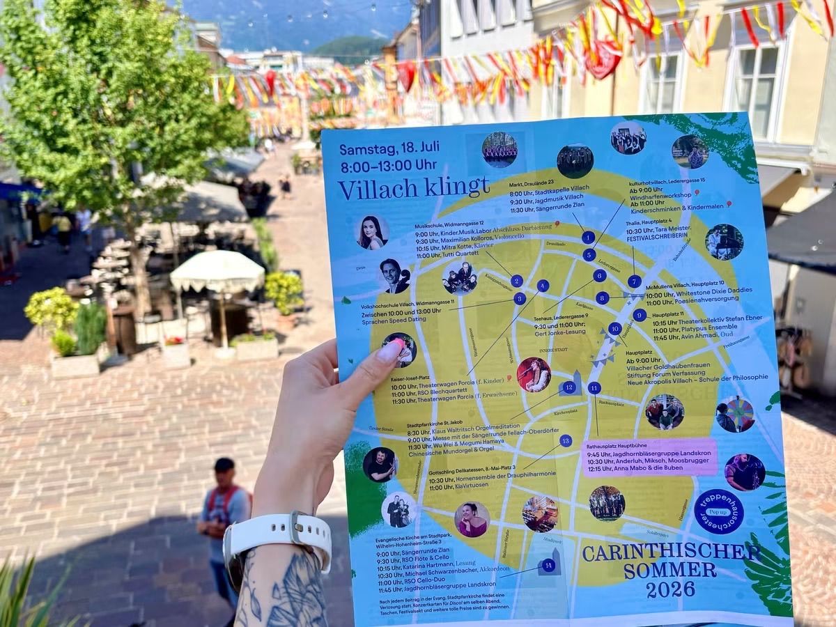 Eine Person hält ein buntes Veranstaltungsflyer für den Kärntner Sommer 2026 in Villach, Österreich. Der Flyer zeigt eine Karte mit verschiedenen Veranstaltungsorten und Zeiten.