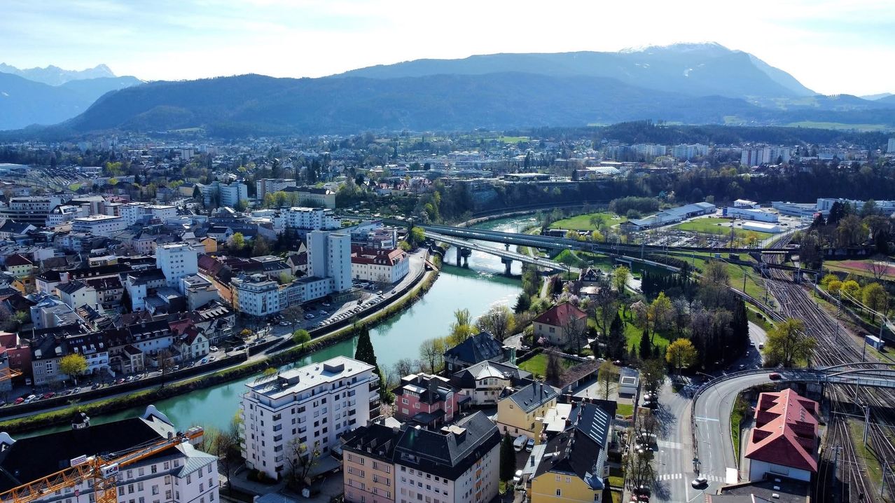 Aerial view of a city with buildings, a river, and a bridge surrounded by mountains.