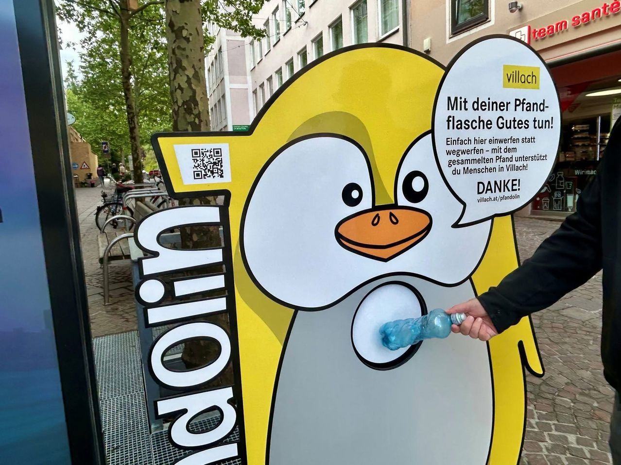 A penguin-shaped sign encourages people to deposit bottles instead of throwing them away. It shows a hand inserting a bottle into the penguin's mouth.