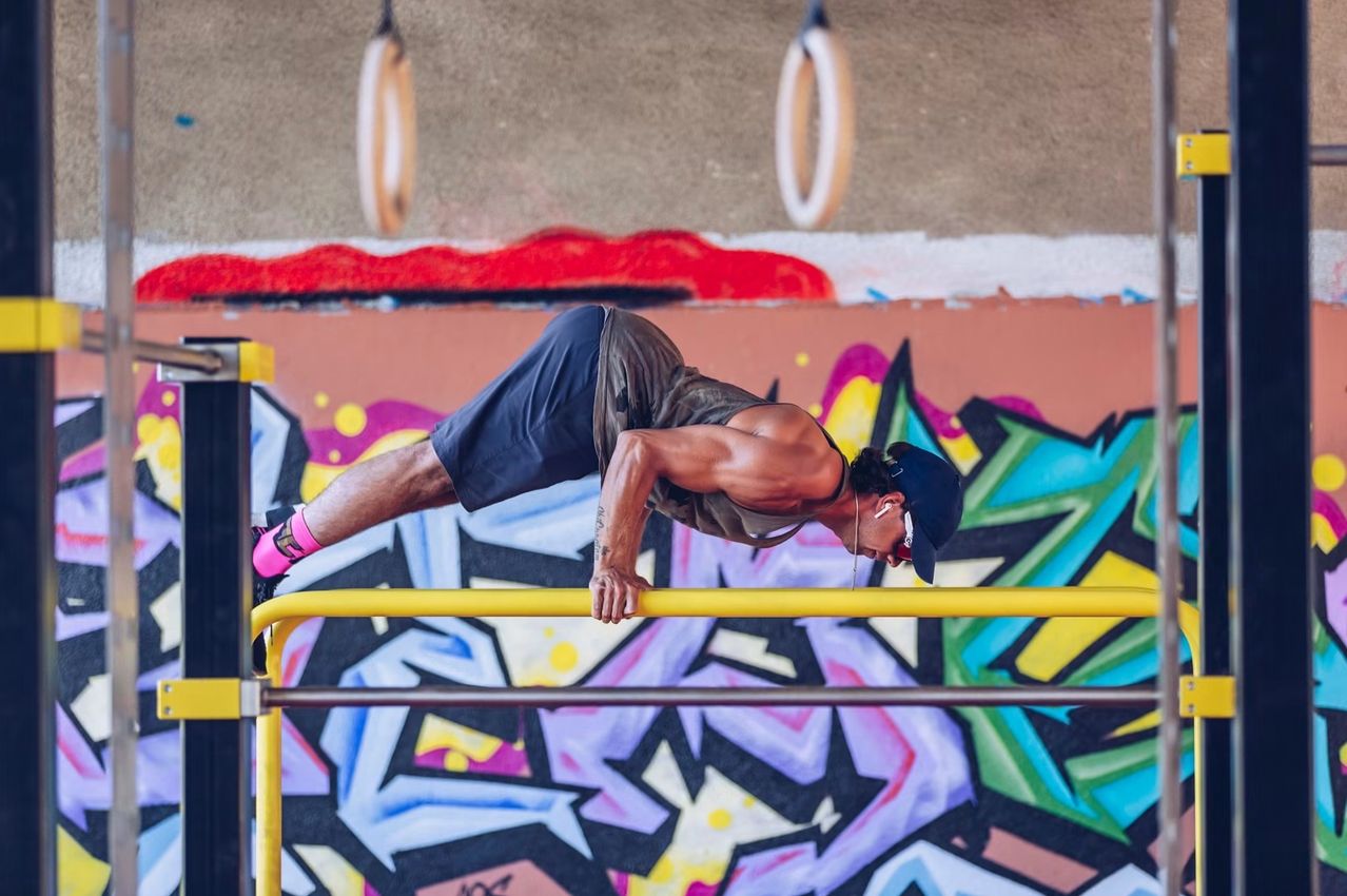 Ein Mann macht Klimmzüge an einer gelben Stange vor einer mit Graffiti bedeckten Wand.