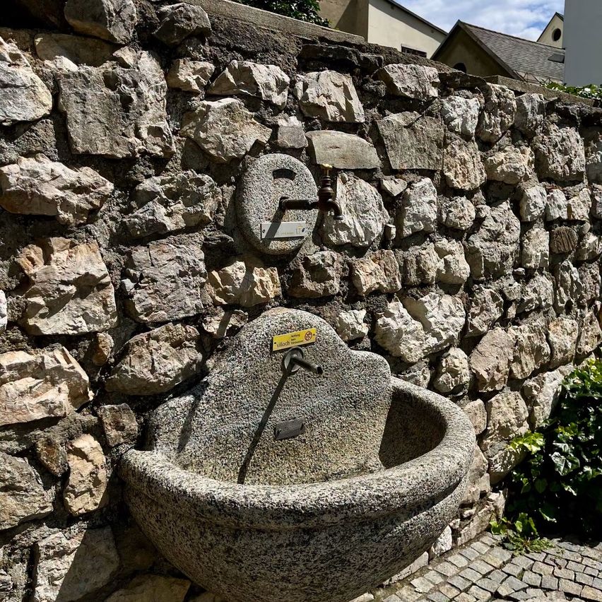 Eine Steinmauer mit einem alten Steinbecken, das daran befestigt ist. Es gibt einen gelben Aufkleber mit dem Wort 'Mühle' darauf.