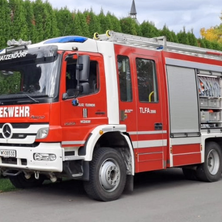 Ein roter Mercedes Benz Feuerwehrwagen steht auf der Straße mit Büschen und Bäumen im Hintergrund.