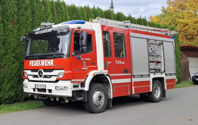 Ein roter Mercedes Benz Feuerwehrwagen steht auf der Straße mit Büschen und Bäumen im Hintergrund.