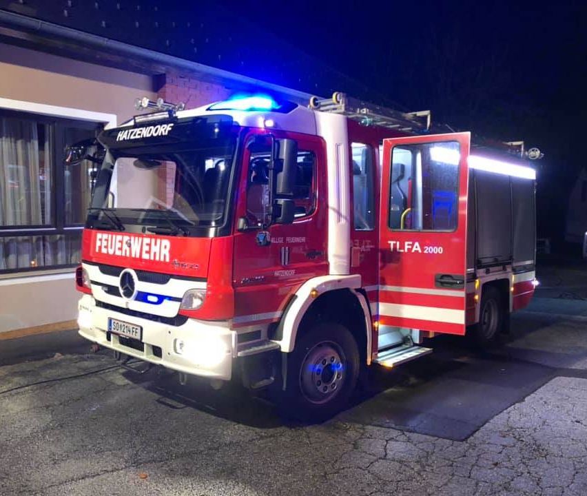 Ein roter Feuerwehrwagen mit der Aufschrift 'FEUEWEHR' und 'HATZENDORF' steht vor einem Gebäude. Das Kennzeichen lautet 'SO/214 FF'.