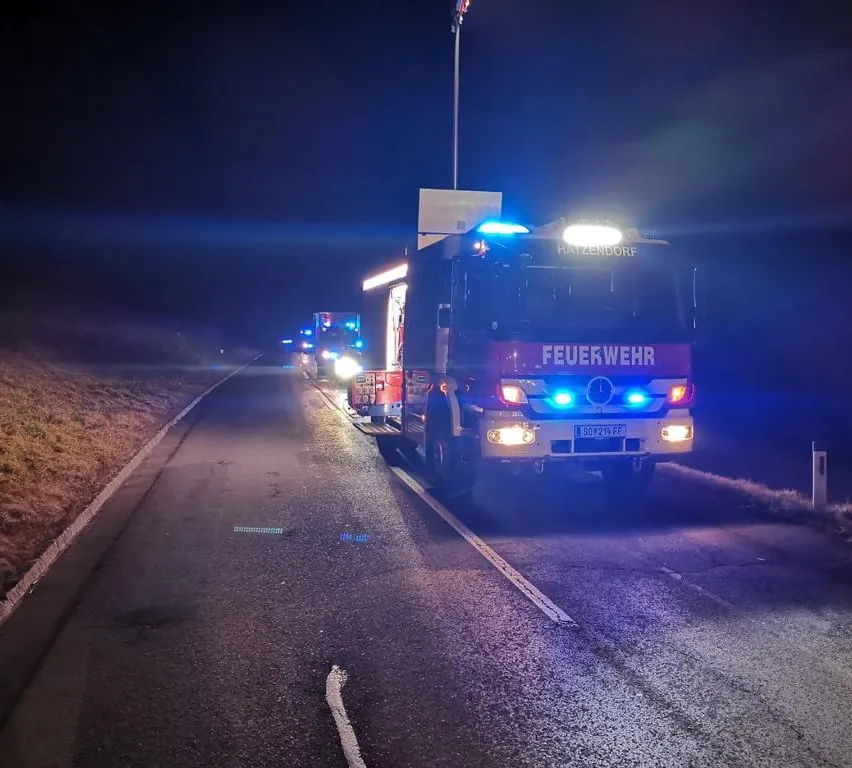 Feuerwehrfahrzeuge stehen bei Nacht mit eingeschalteten Lichtern am Straßenrand.