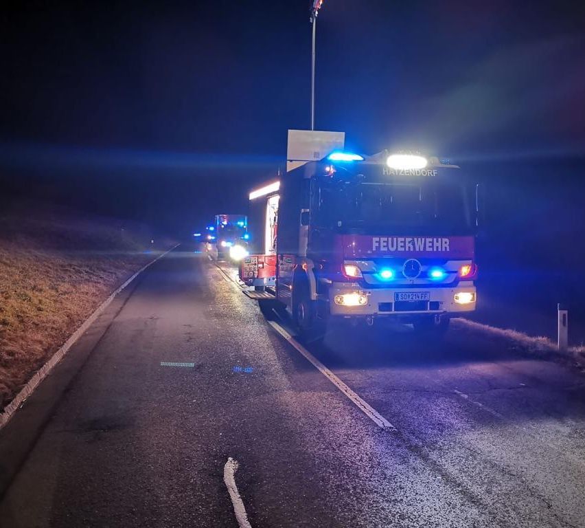 Feuerwehrfahrzeuge stehen bei Nacht mit eingeschalteten Lichtern am Straßenrand.