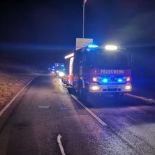 Feuerwehrfahrzeuge stehen bei Nacht mit eingeschalteten Lichtern am Straßenrand.