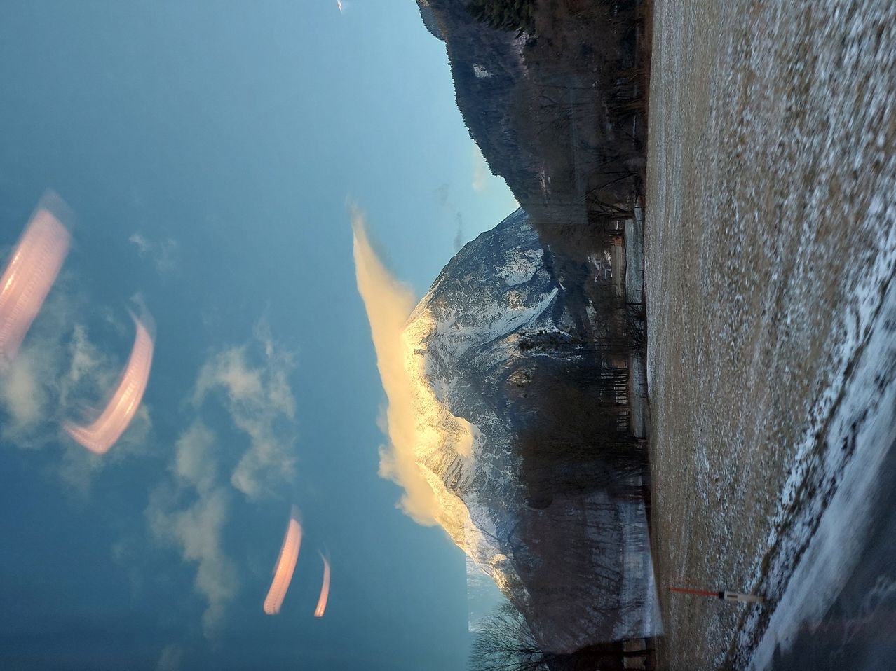 Eine Berglandschaft mit schneebedeckten Gipfeln unter einem klaren blauen Himmel. Drei Paraglider sind im Himmel zu sehen.