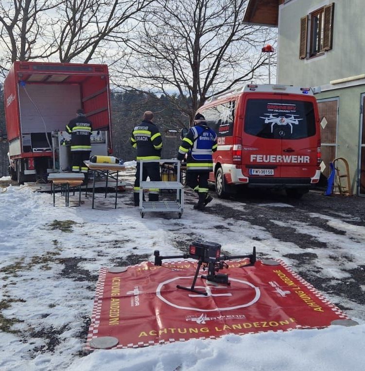 Feuerwehrleute bereiten einen Drohnenflug auf einem verschneiten Gebiet vor, in der Nähe eines Feuerwehrwagens und eines Transporters mit Ausrüstung.