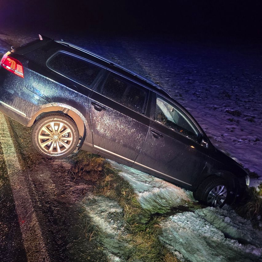 Ein schwarzer SUV liegt auf der Seite auf einer verschneiten Straße bei Nacht. Die Scheinwerfer des Fahrzeugs sind eingeschaltet und beleuchten die Szene.