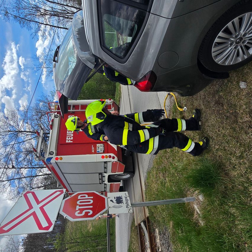 Feuerwehrleute arbeiten an einem Auto neben einem Stoppschild an einem sonnigen Tag.