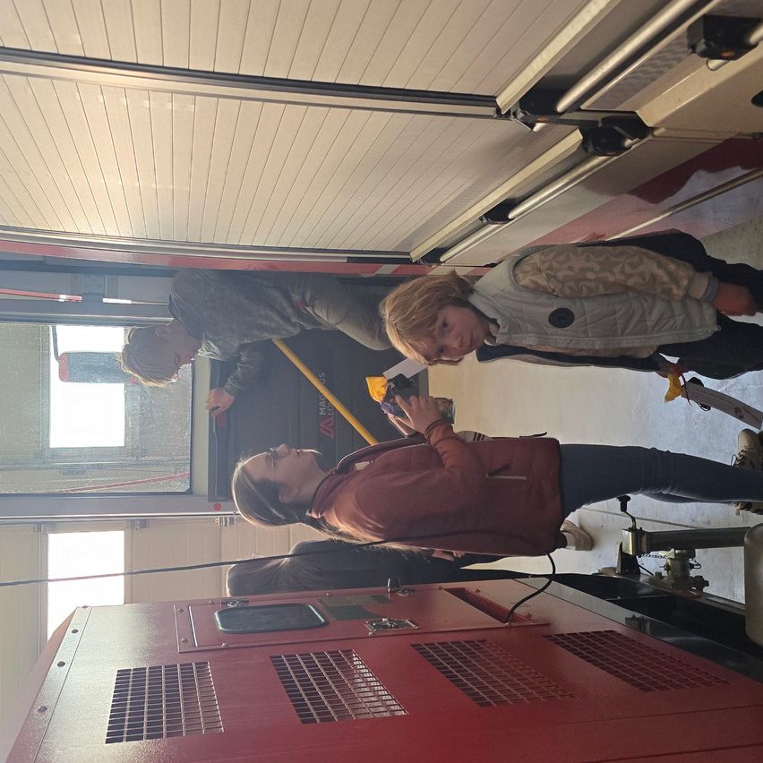 Drei Personen sind in einem Feuerwehrauto und schauen durch das Fenster nach draußen. Eine macht ein Foto.