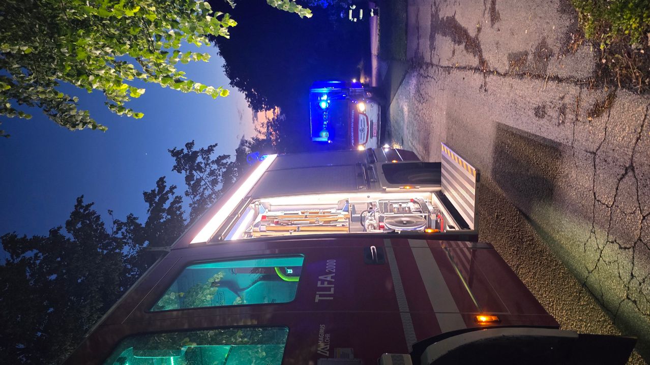Eine obere Ansicht eines Feuerwehrwagens mit offener Hecktür, blinkenden Lichtern, geparkt am Straßenrand in der Dämmerung.