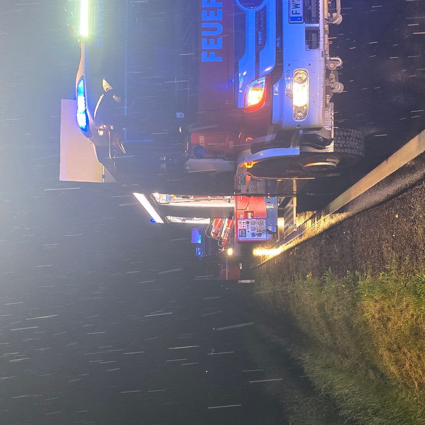Ein Feuerwehrfahrzeug steht nachts mit eingeschalteten Lichtern am Straßenrand. Es trägt den Schriftzug 'Feuerwehr' an der Seite.