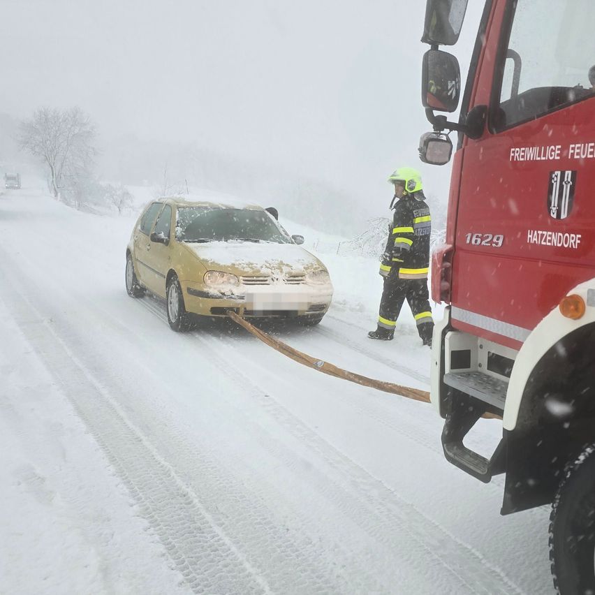 Ein Feuerwehrmann hilft einem gelben Auto, das im Schnee feststeckt, mit einem Seil auf einer verschneiten Straße.