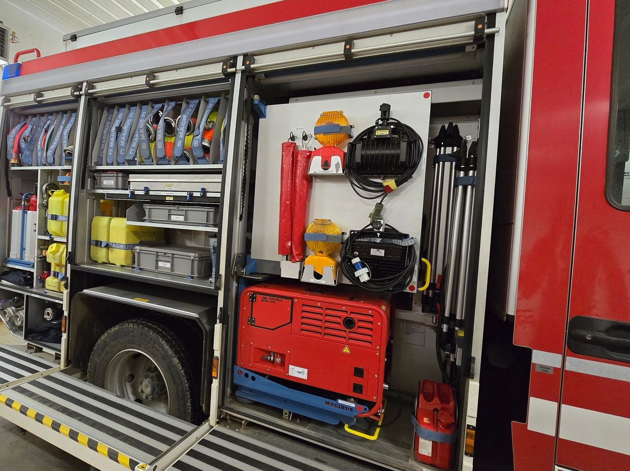 Der Innenraum eines Feuerwehrfahrzeuges ist offen und zeigt einen roten Generator und eine Sammlung von Werkzeugen und Ausrüstung. Aufbewahrungsboxen und Container sind auf den Regalen.